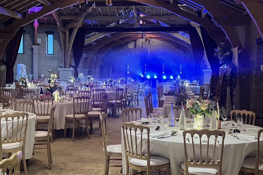 Grande salle à poutres du Château Montus dressée pour un mariage, lustres et piste de danse éclairée en bleu
