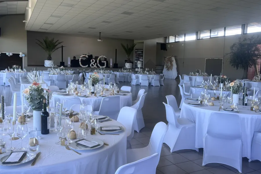 Salle des fêtes de Horgues dressée pour un mariage, tables rondes nappes blanches et scène avec régie DJ au fond