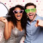 Deux invités posant avec des accessoires devant le photobooth lors d’une soirée